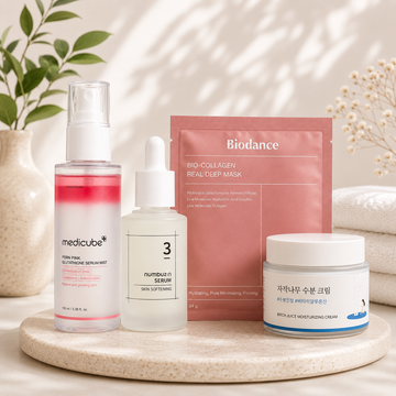 Skincare products including a bottle, serum, mask, and cream on a wooden tray with a neutral background.